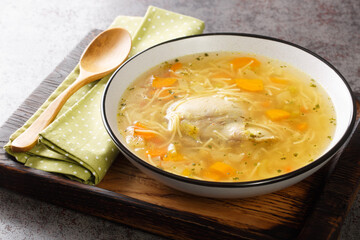 Polish Rosol z kury chicken soup with vermicelli and vegetables close-up in a bowl on a wooden tray on the table. horizontal