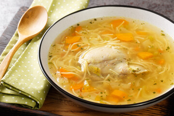 Dietary chicken soup with vermicelli and vegetables close-up in a bowl on a wooden tray on the table. horizontal © FomaA