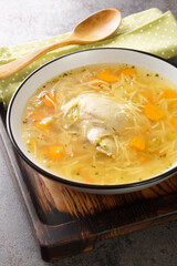 Chicken broth with noodles and vegetables close-up in a plate on a wooden tray. Vertical © FomaA