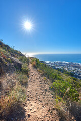 Fototapeta na wymiar Remote mountain hiking trail on table mountain on a sunny day. Mountainous walking path high above a coastal city in South Africa against a blue horizon. Popular tourist attraction in Cape Town