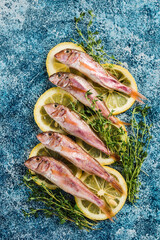 Some fresh Black Sea red mullet with lemon slices and fresh thyme on a blue background.