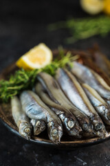 Pickled capelin with a slice of lemon and thyme on a metal plate on a dark background.