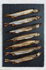 Smoked capelin on a black graphite board on a light background.
