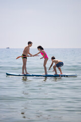 Three kids enyoying with a paddle surf in the sea on a summer day