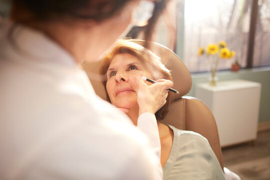 Female doctor drawing correction lines on woman's face 