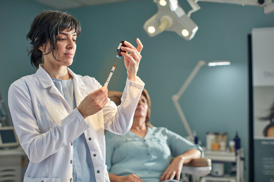 Female doctor preparing botox injection, patient in background