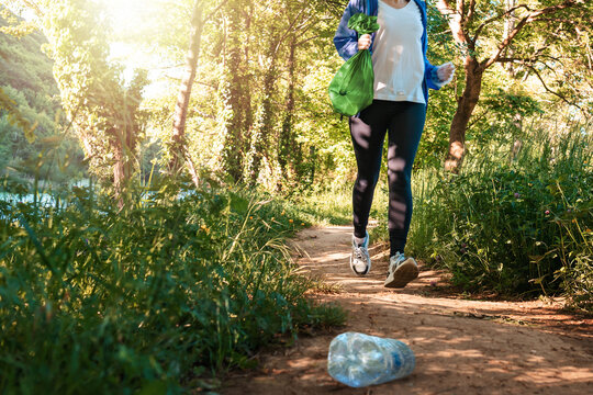 Person in sportswear jogging at the park and holding a bag of garbage. Low angle view. The concept of environmental protection, plogging and volunteering