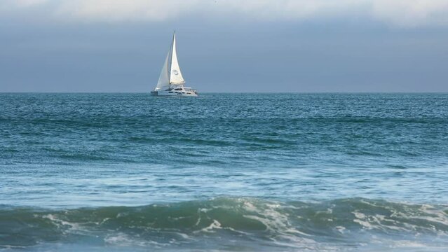 side view of Catamaran sailboat sailing in full sail on a dark blue sea with reflections in backlight