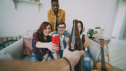 POV shot of male hand clinking beer bottle with friends while celebrating party at home