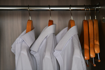 A lot of white male shirts hanged inside a dressing wardrobe. Man office clothing industry.