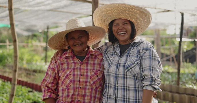 Happy Asian woman farmers looking to camera and laughing together on local organic vegetable farm.