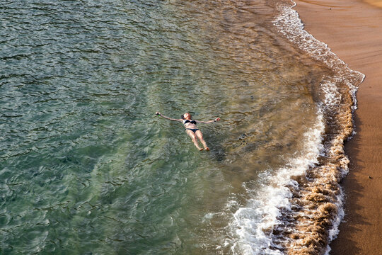 top view of woman floating in the sea near sandy beach