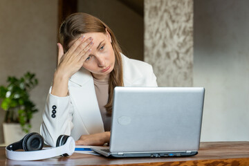 Feeling tired and stressed. Upset young woman in a white jacket massaging her nose while sitting at...