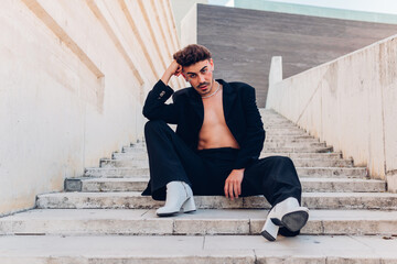 Full body of feminine male with rhinestones on face in high heeled boots looking at camera while...