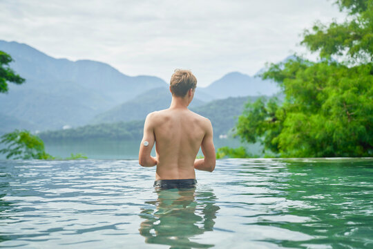 Diabetes Patient In A Swimmingpool With An Waterproof CGM (Continuous Glucose Monitor) Device To Measure Real-time Blood Sugar For A Healthy Lifestyle Without Setbacks For A Good Healthcare.