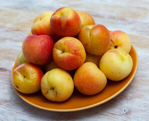 Pile of ripe sweet apricots on plate on wooden table. Healthy vitamin fruits