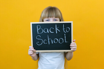 schoolgirl holding a tablet in her hands with the inscription Back to school on a yellow background.