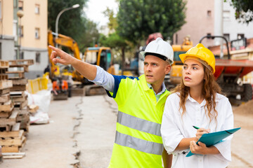 Contractor working on a construction site shows something to a young woman engineer controlling the progress of work, ..pointing it out