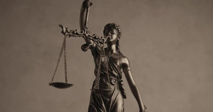 justice by blindfolded bronze law statue with sword and balance spinning in front of brown background illustrating concept of power and rights