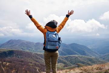 Young woman with rucksack and arms wide opened on the top of the hilly landscape.