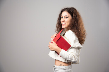 Young woman holding red book on a gray wall