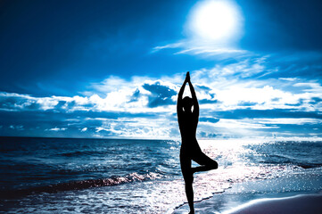 Silhouette of woman in tree pose of yoga. Sun sky and sea. Concept of calm and harmony.