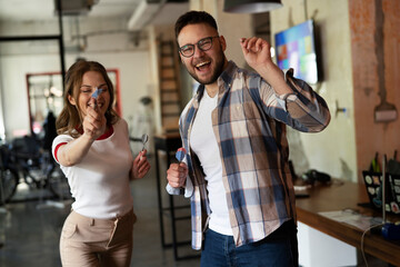 Young colleagues taking break after work. Happy young businessman and businesswoman playing darts in the office.