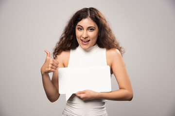 Fototapeta premium Young woman showing a thumb up and holding blank white poster