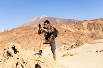 Fototapeta premium Young man taking pictures on a road trip. Man making memories on the mountain..