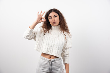 Obraz premium Young woman showing ok gesture in white sweater with curly hair