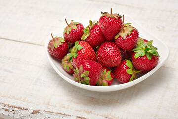 strawberries in a plate on a white wooden background, fresh red berries, concept of fresh fruits and healthy food