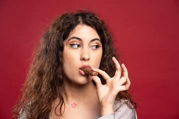 Elegant woman eating chocolate on red background