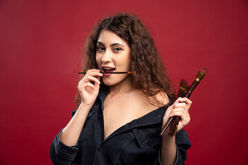 Obraz premium Young artist posing with paintbrushes on red background