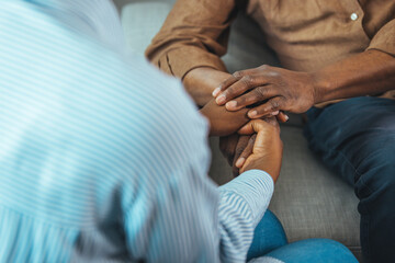 Close up black woman and man sitting on couch two people holding hands. Symbol sign sincere...