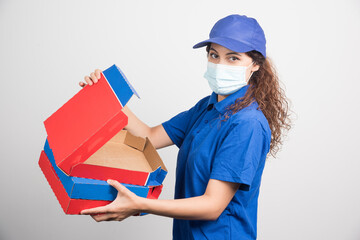 Fototapeta na wymiar Pizza delivery girl opening one of the boxes of pizza with medical facemask on white background