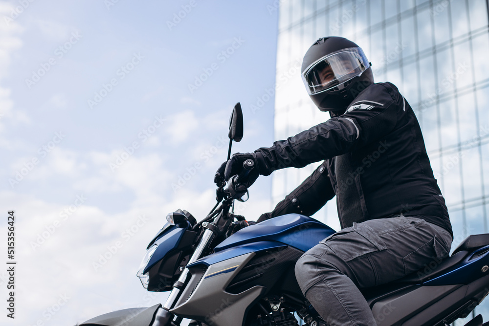 Wall mural Handsome motorcyclist on his moto riding in the city