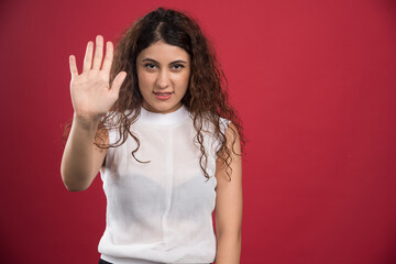 Woman with curly hair doing stop sing on red background