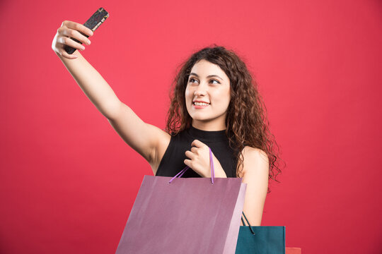 Woman doing selfie with bags on red background