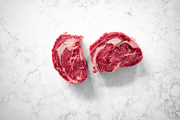 two cuts of rib-eye steak on a marble counter top