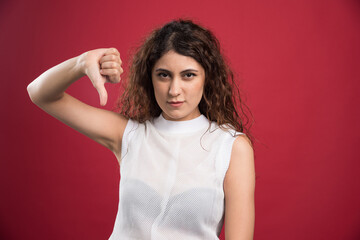 Young woman showing thumbs down sign to dislike on red background