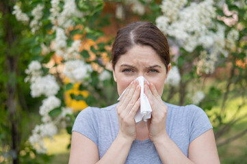 Caucasian woman suffers from allergies and blows her nose into a napkin while walking in the park. 
