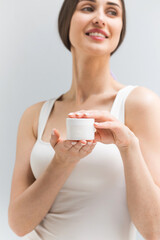 Smiling woman shows jar of moisturizing cream on light background in studio