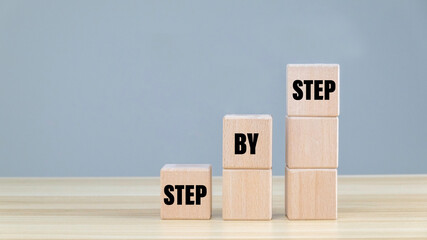 Hand arranging wood block stacking as step stair on top with word Step By Step. Business concept...