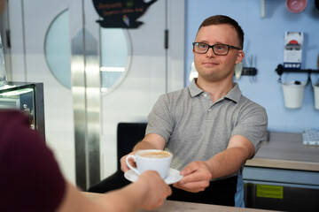 Caucasian man with down syndrome serving a cup of coffee  to the client