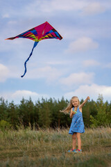 In summer, a girl is flying a kite on the field. Plays outdoors in the park at sunset. The child plays in nature.