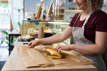 Young caucasian waitress packing prepared sandwich in commercial kitchen - Powered by Adobe