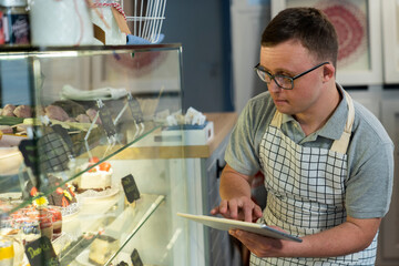 Caucasian man with down syndrome doing fridge inventory in a cafe using digital tablet
