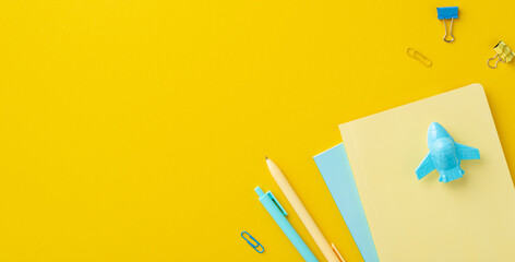 Back to school concept. Top view photo of stationery airplane shaped sharpener over notebooks binder clips and pens on isolated yellow background with copyspace