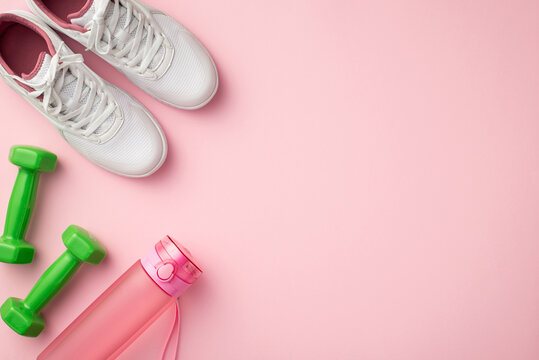 Fitness accessories concept. Top view photo of white sneakers pink bottle and green dumbbells on isolated pastel pink background with copyspace