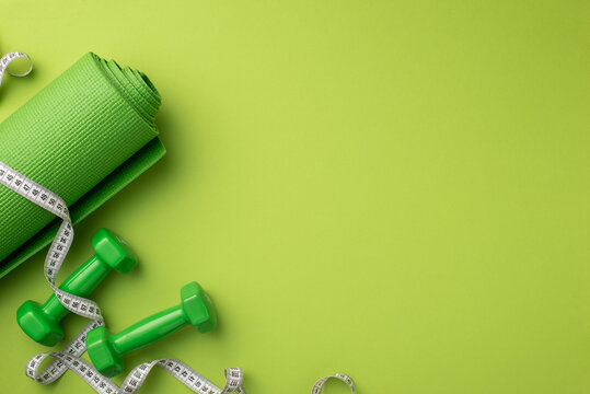 Sports concept. Top view photo of green exercise mat tape measure and dumbbells on isolated green background with empty space